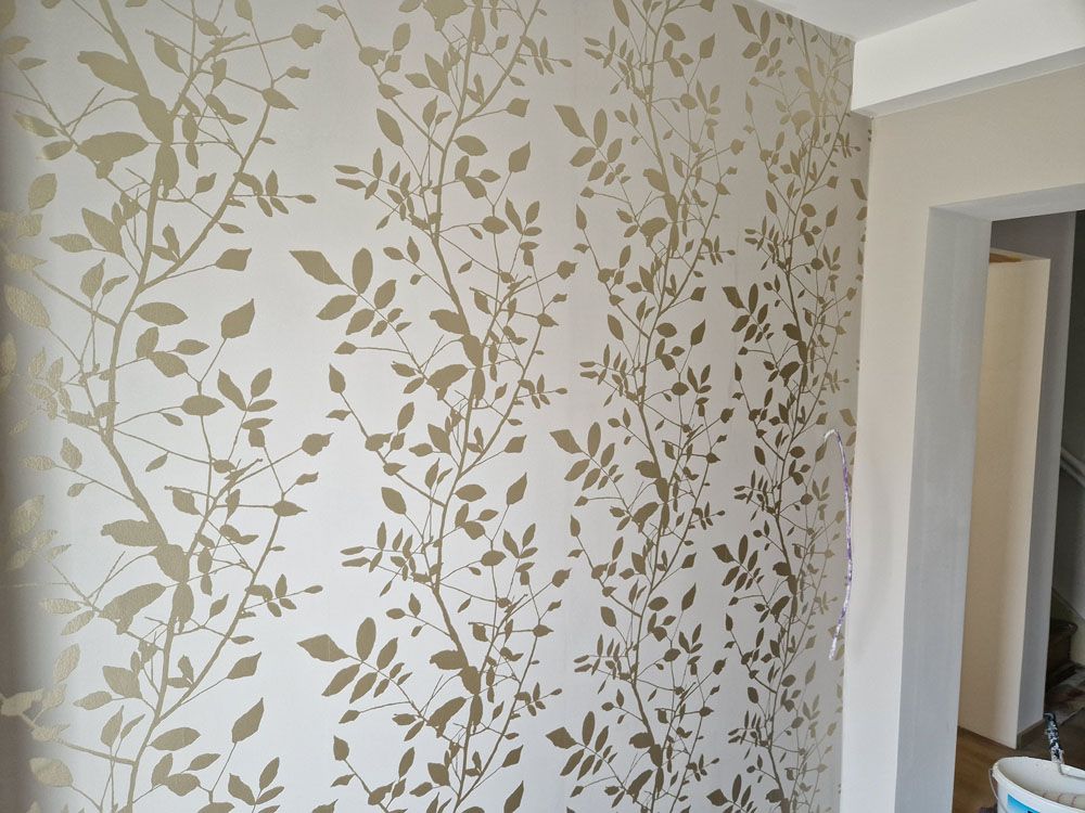 Beige Wand mit goldenen, vertikal verlaufenden Blätterranken und hellem Licht
