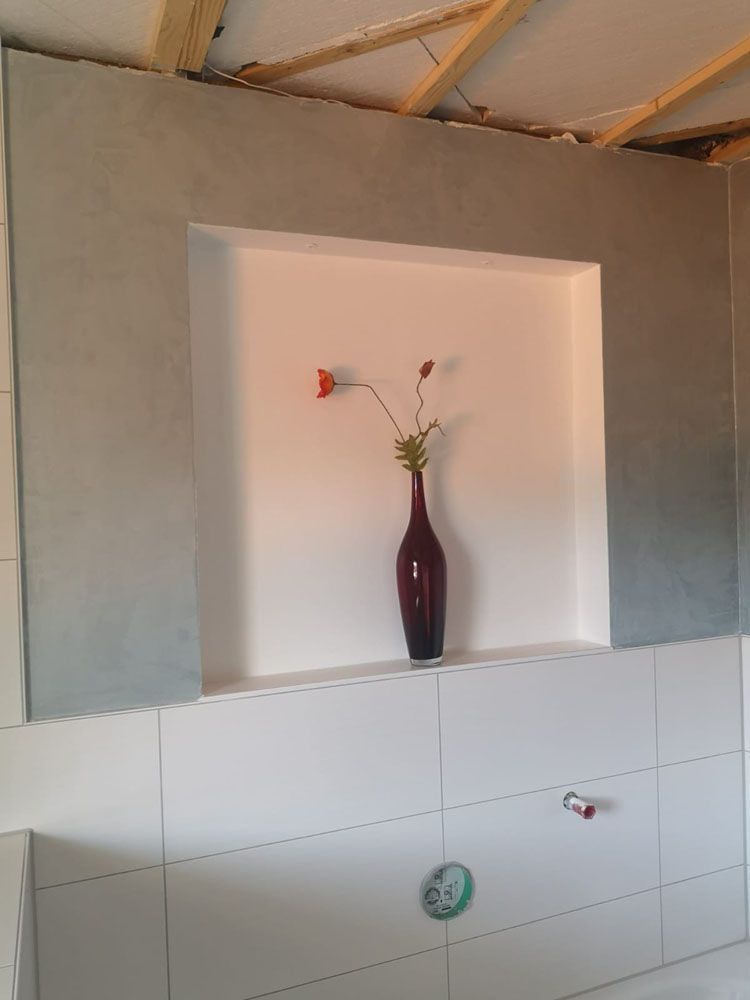 Eine rote Vase mit kunstvollen Blumen steht in einer Wandnische mit grauem Rahmen