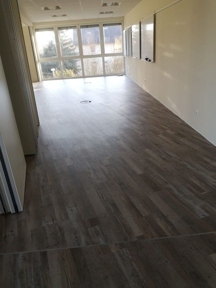 Ein leerer, heller Raum mit Holzboden, weißen Wänden und großen Fenstern