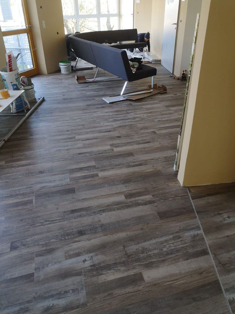 Helles Wohnzimmer mit Laminatboden, dunklem Sofa und Malerutensilien im Hintergrund