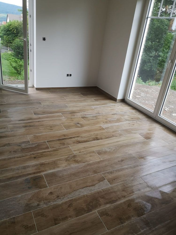 Helles Zimmer mit großen Fenstern und braun gemasertem Fliesenboden
