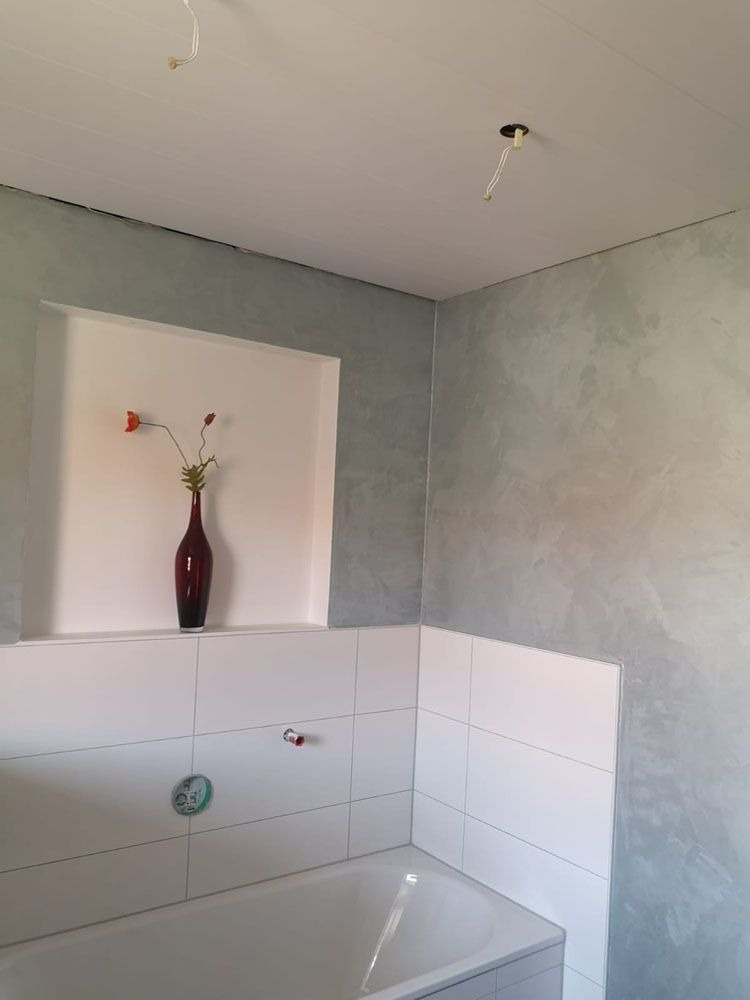 Ein Badezimmer mit weißen Fliesen, einer grauen Wand und einer roten Vase mit Blume
