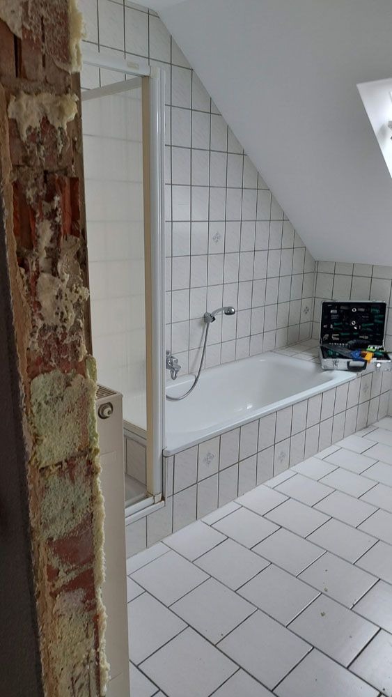Ein hell gefliestes Badezimmer mit Badewanne, auf der Werkzeuge liegen