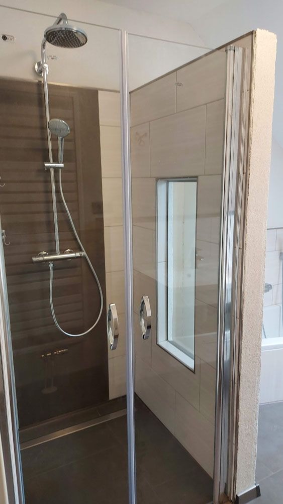 Eine moderne Duschkabine mit Glastüren und silbernen Armaturen in grauen Tönen