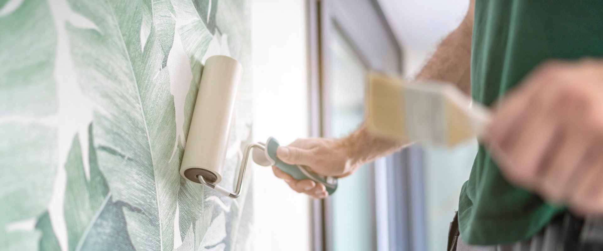 Maler drückt die frisch verklebte Mustertapete mit der Rolle an die Wand